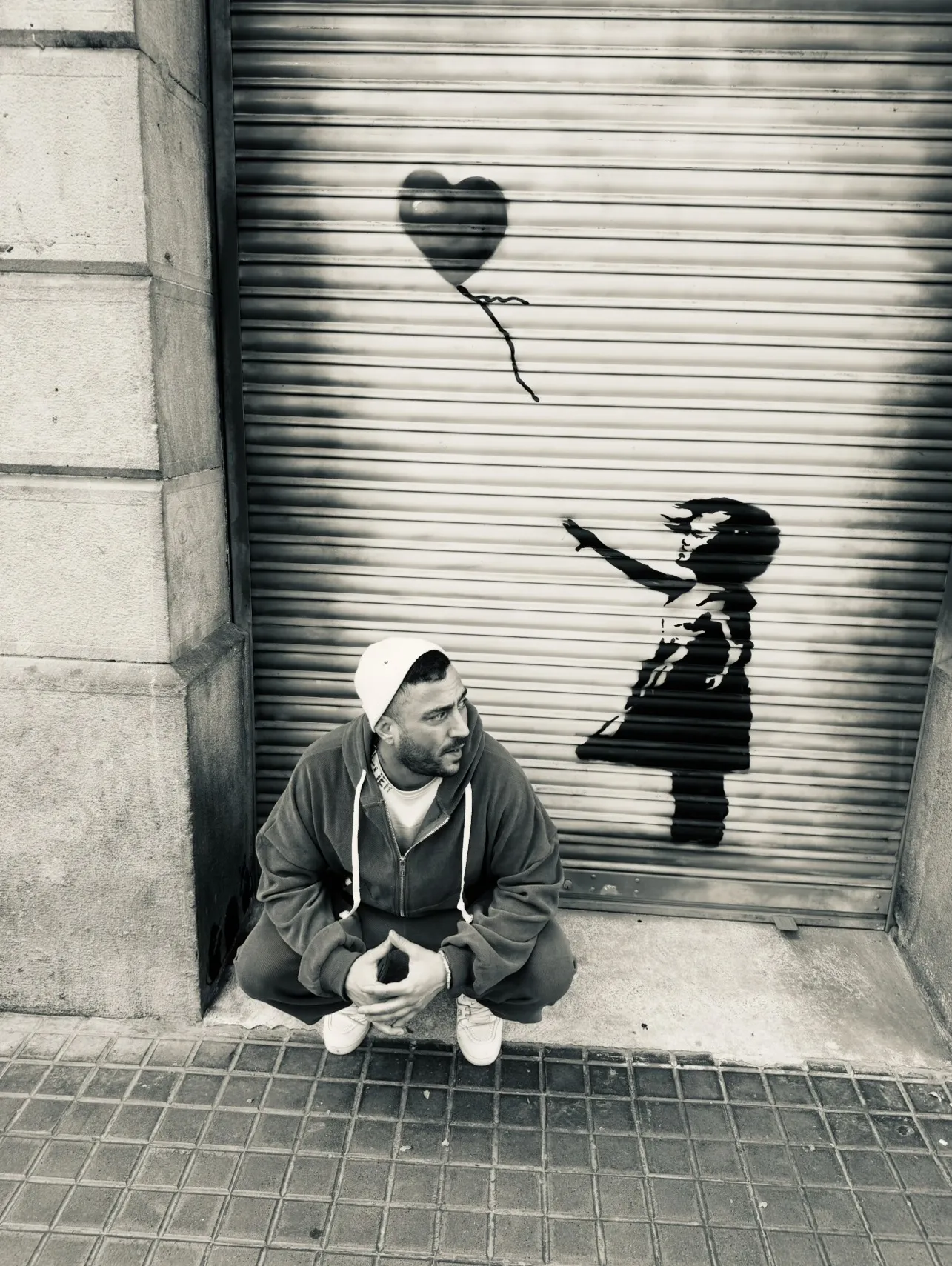 Tas sitzt vor einem Banksy-Wandbild mit Mädchen und Herzballon