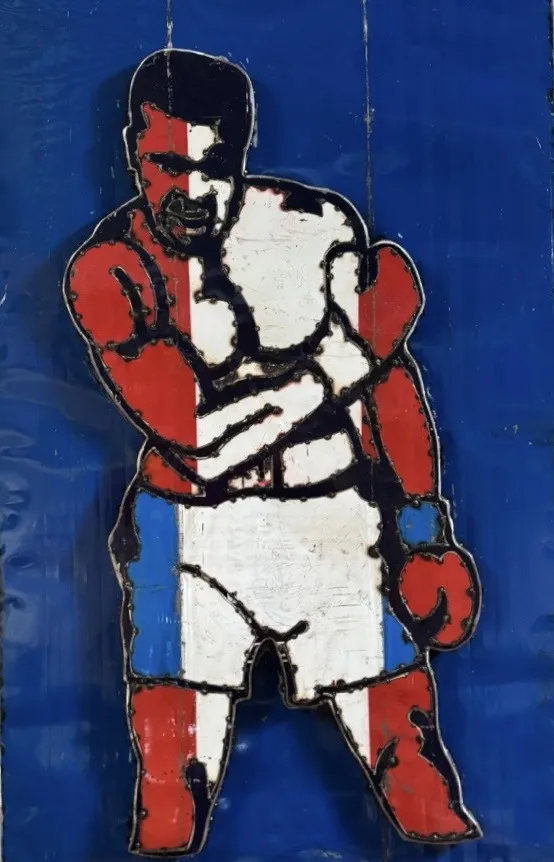 Stahlbild von Muhammad Ali in Boxpose, weiß-rote Figur auf blauem Metallgrund